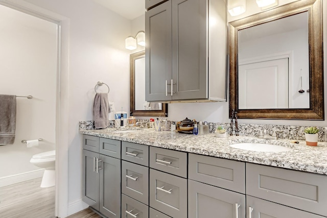 bathroom with double vanity, baseboards, toilet, wood finished floors, and a sink