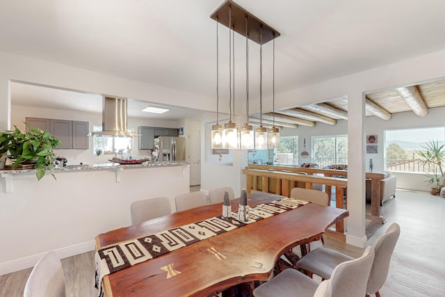 dining area featuring light wood-type flooring, beam ceiling, and baseboards