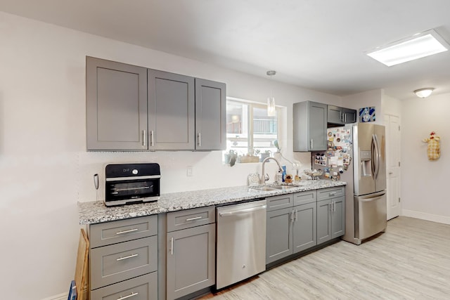 kitchen featuring stainless steel appliances, a sink, baseboards, light wood-type flooring, and gray cabinets