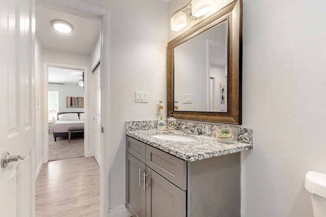 half bath with toilet, ceiling fan, vanity, wood finished floors, and baseboards