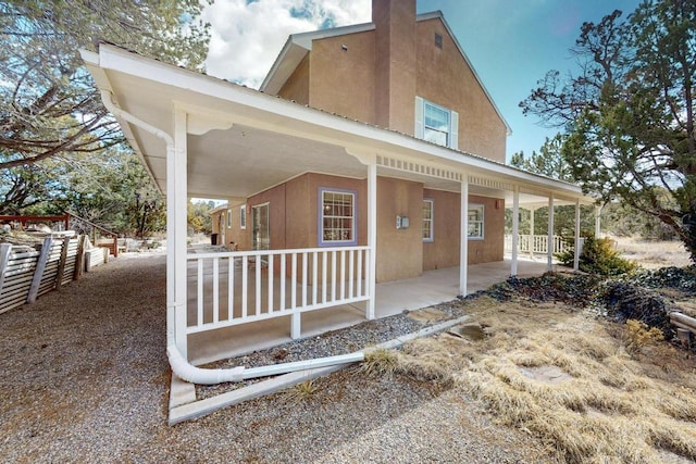 rear view of house featuring a chimney, fence, covered porch, and stucco siding