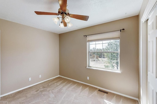 empty room featuring light carpet, visible vents, a ceiling fan, and baseboards