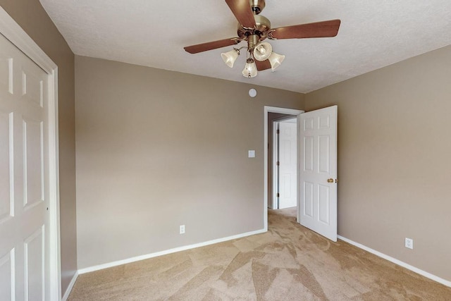 unfurnished bedroom with light colored carpet, a textured ceiling, a ceiling fan, and baseboards