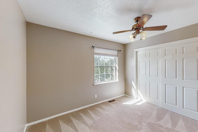 unfurnished bedroom featuring a textured ceiling, baseboards, a closet, and light carpet