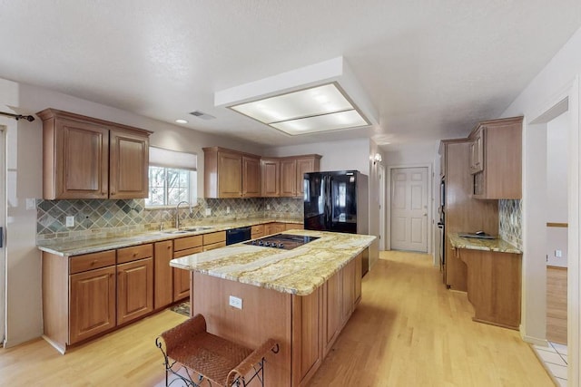 kitchen with a sink, light wood-type flooring, a kitchen island, and black appliances