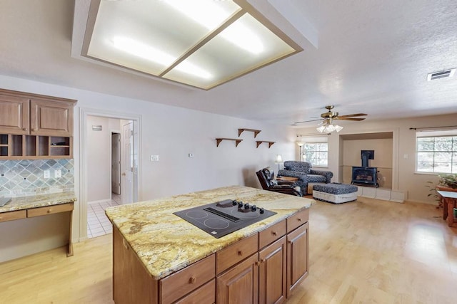 kitchen with a wealth of natural light, light wood-type flooring, visible vents, black electric cooktop, and a wood stove