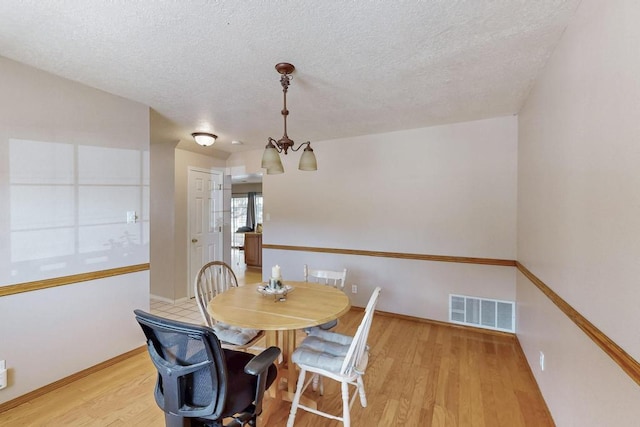 dining area with a textured ceiling, baseboards, visible vents, and light wood-type flooring