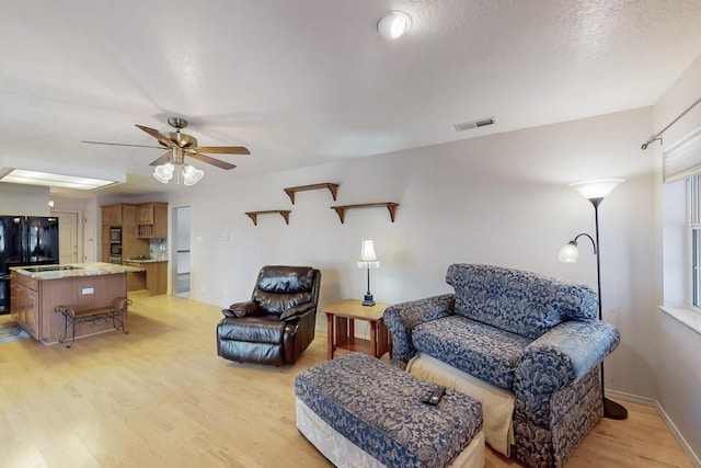 living room featuring visible vents, ceiling fan, baseboards, and light wood-style floors