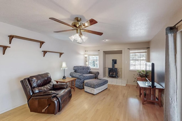 living area with baseboards, a wood stove, a ceiling fan, and wood finished floors