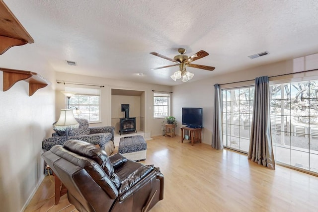 living room with visible vents, a ceiling fan, light wood-style flooring, and a wood stove