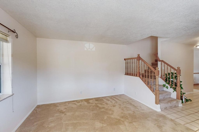 carpeted spare room with stairs, baseboards, and a textured ceiling