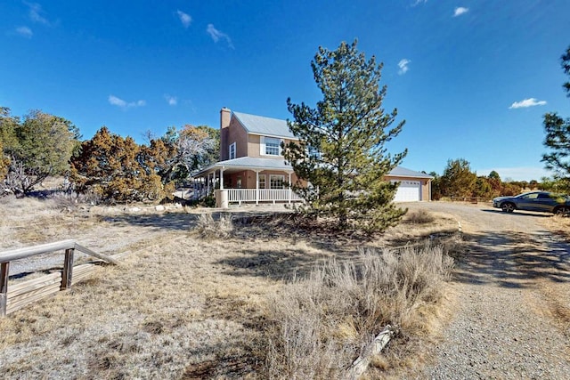 view of front of property with covered porch, a chimney, metal roof, a garage, and driveway