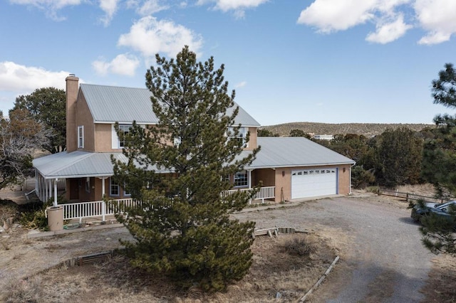 view of front facade with covered porch, a chimney, a garage, dirt driveway, and metal roof