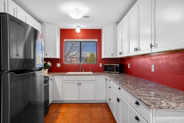 kitchen with light tile patterned floors, stainless steel microwave, freestanding refrigerator, white cabinets, and a sink