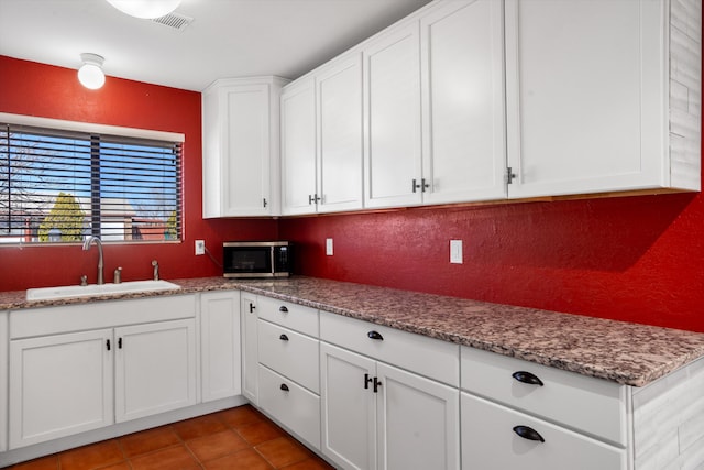 kitchen featuring light tile patterned flooring, a sink, visible vents, white cabinets, and stainless steel microwave