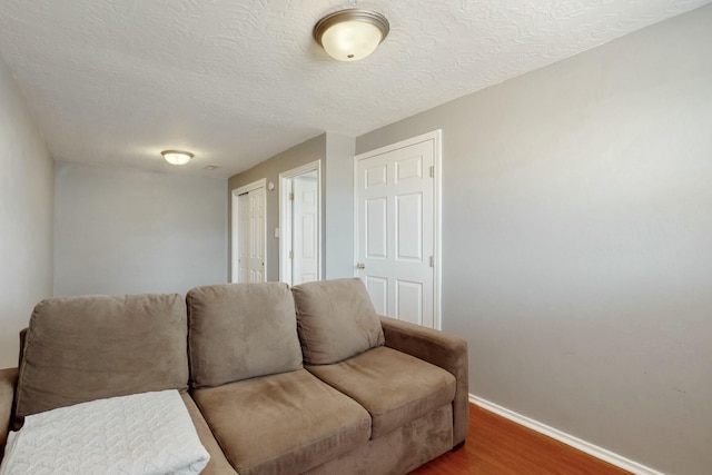 living room featuring a textured ceiling, baseboards, and wood finished floors