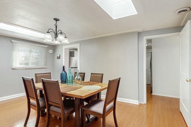 dining space featuring light wood-style flooring, an inviting chandelier, visible vents, and baseboards