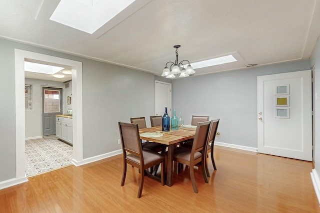 dining room featuring light wood-style floors, a skylight, a chandelier, and baseboards