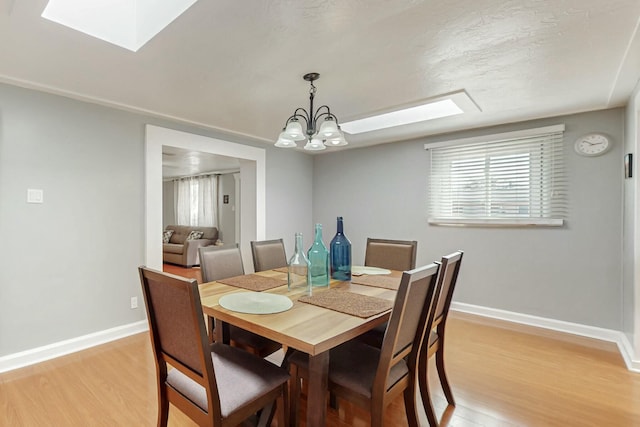 dining area with light wood-type flooring, a skylight, baseboards, and a chandelier