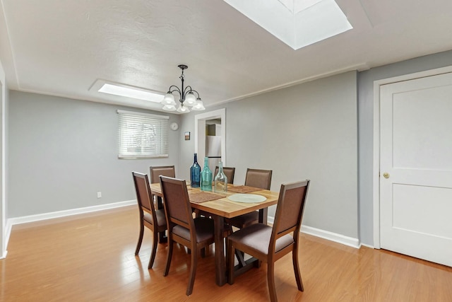 dining area featuring an inviting chandelier, light wood-style flooring, a skylight, and baseboards