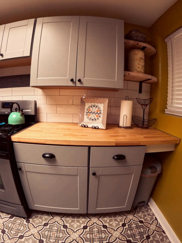 kitchen featuring light tile patterned flooring, gray cabinetry, butcher block countertops, range, and decorative backsplash