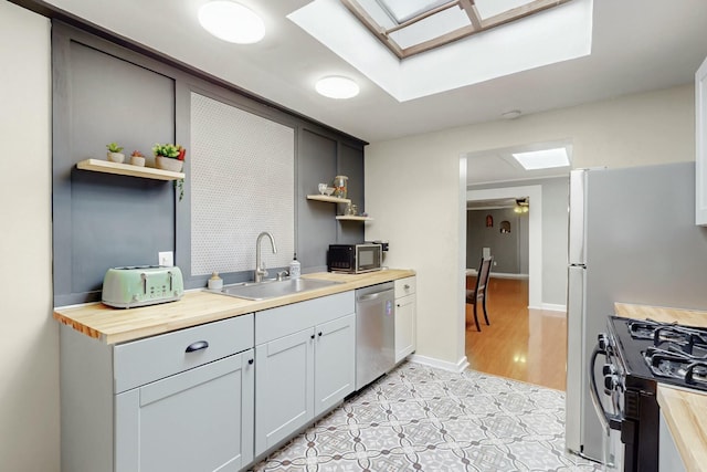 kitchen featuring stainless steel appliances, open shelves, a skylight, and a sink