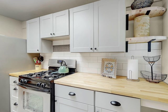 kitchen featuring butcher block counters, stainless steel range with gas cooktop, white cabinets, and backsplash