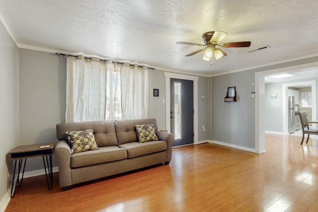 living area featuring light wood-type flooring, visible vents, a textured ceiling, and baseboards