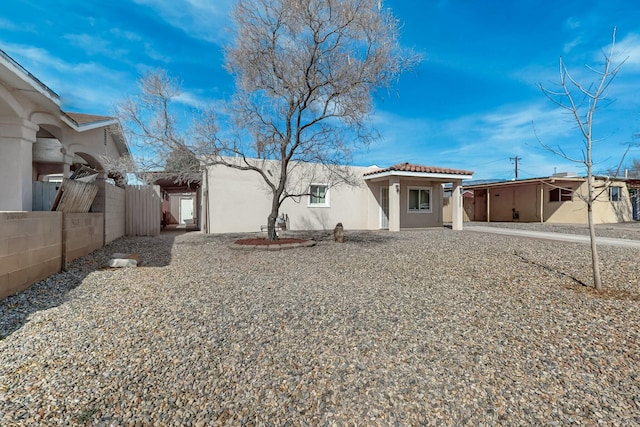 view of front facade with fence, a tile roof, and stucco siding