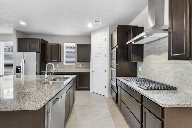 kitchen with visible vents, a sink, dark brown cabinetry, appliances with stainless steel finishes, and wall chimney range hood