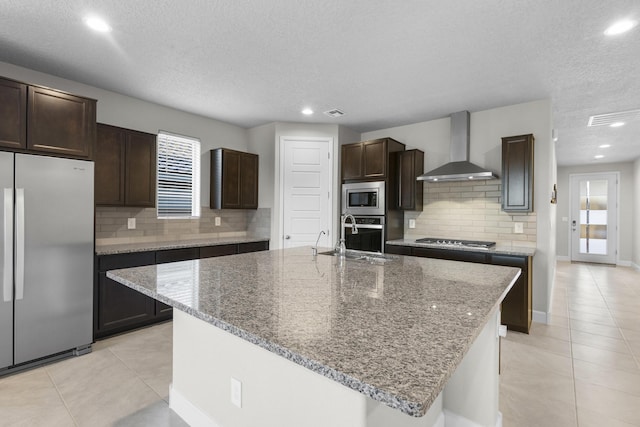 kitchen with wall chimney range hood, light tile patterned floors, appliances with stainless steel finishes, and a sink