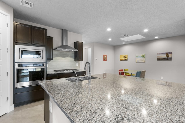 kitchen featuring visible vents, a sink, appliances with stainless steel finishes, wall chimney range hood, and decorative backsplash