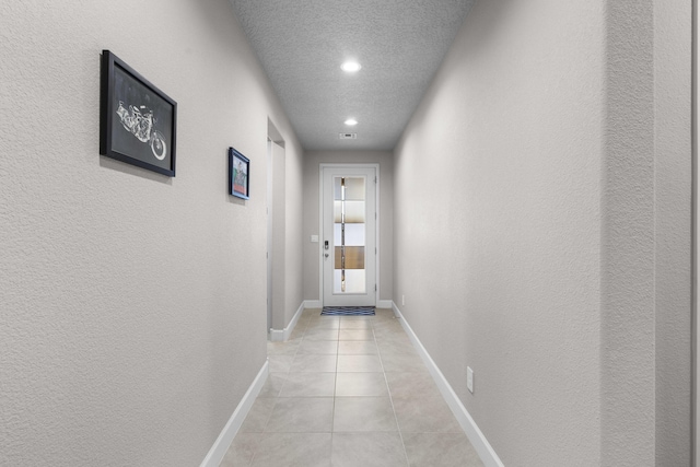 hallway with baseboards, a textured ceiling, light tile patterned flooring, and a textured wall