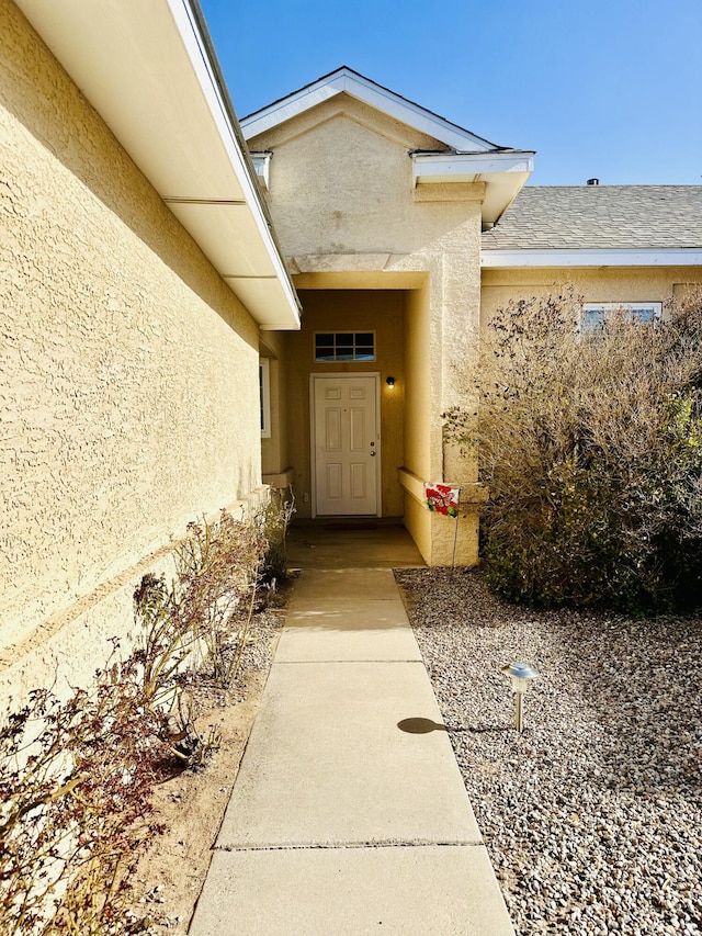 entrance to property with roof with shingles and stucco siding