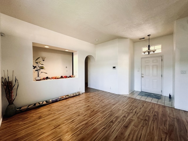 foyer entrance with arched walkways, a notable chandelier, visible vents, a textured ceiling, and wood finished floors