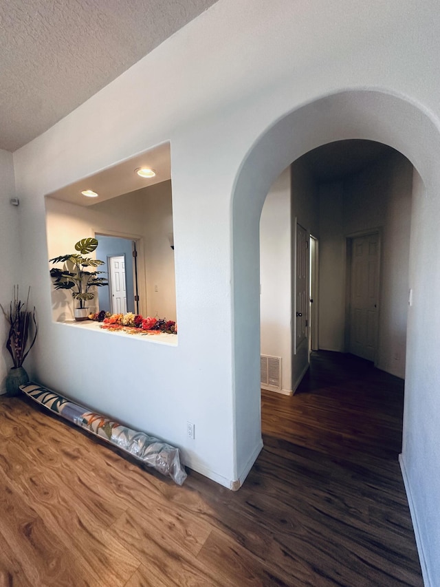 corridor with baseboards, visible vents, arched walkways, wood finished floors, and a textured ceiling