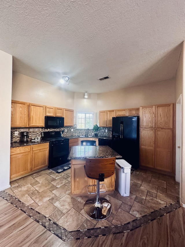 kitchen with a center island, stone tile floors, visible vents, decorative backsplash, and black appliances