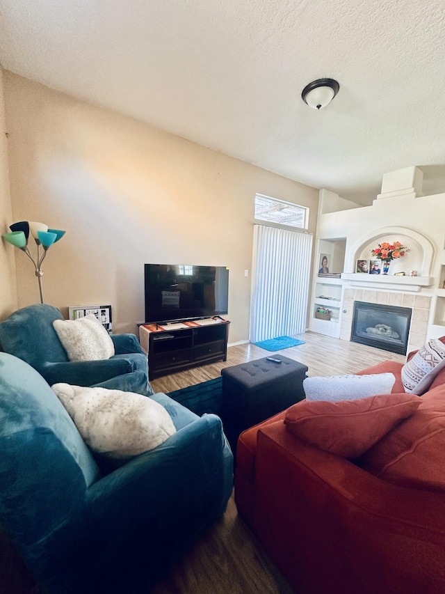 living area with a textured ceiling, built in shelves, a tiled fireplace, and wood finished floors