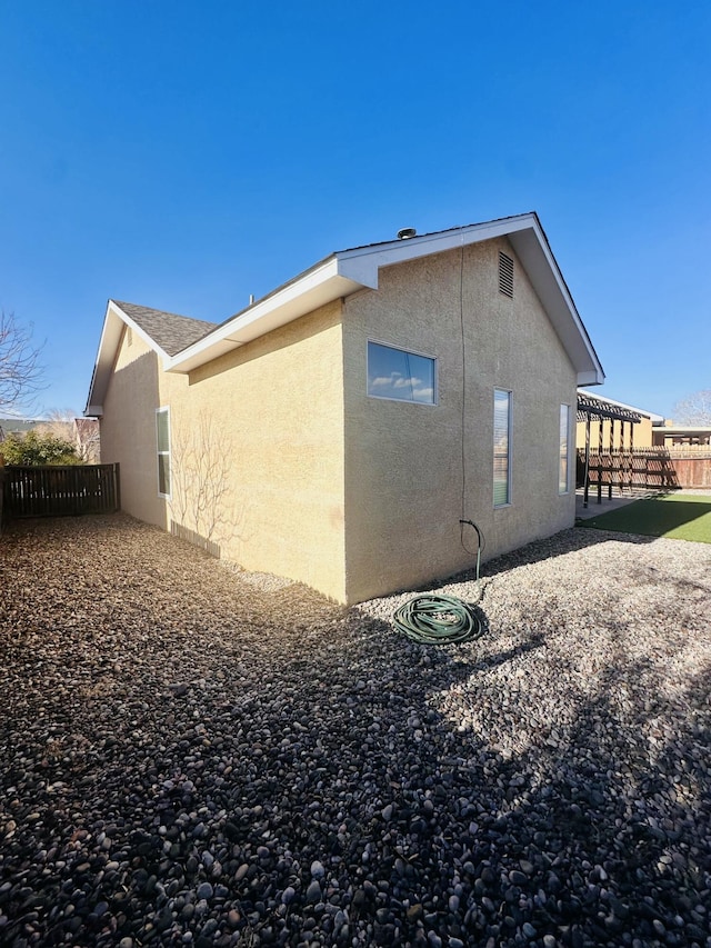 view of side of home featuring roof with shingles, fence, a patio, and stucco siding