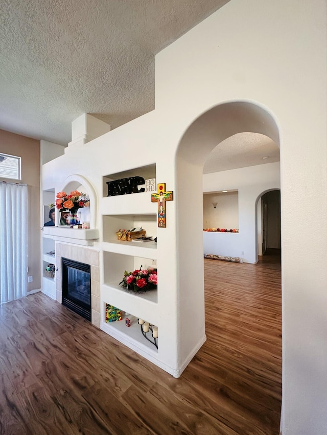 interior space featuring built in features, a textured ceiling, arched walkways, and wood finished floors