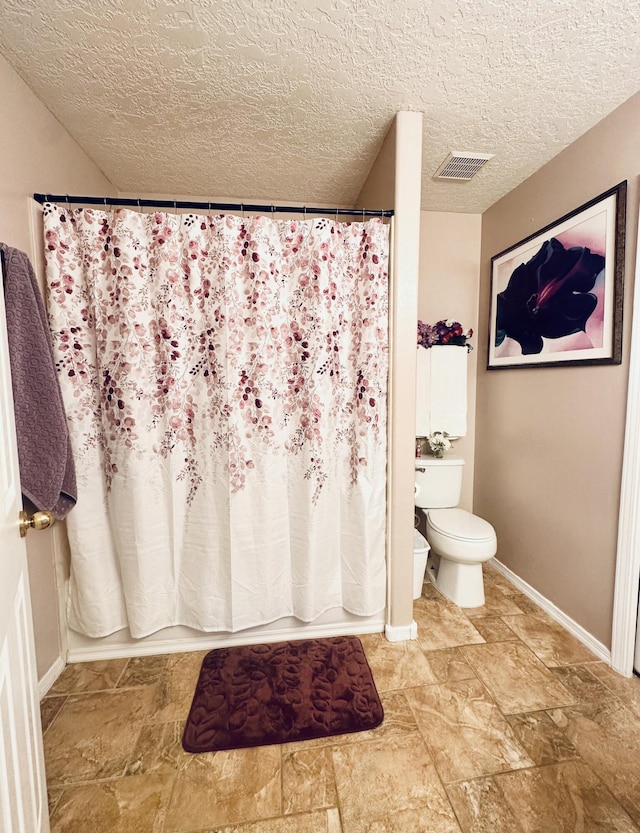 bathroom with a textured ceiling, toilet, visible vents, baseboards, and a shower with curtain