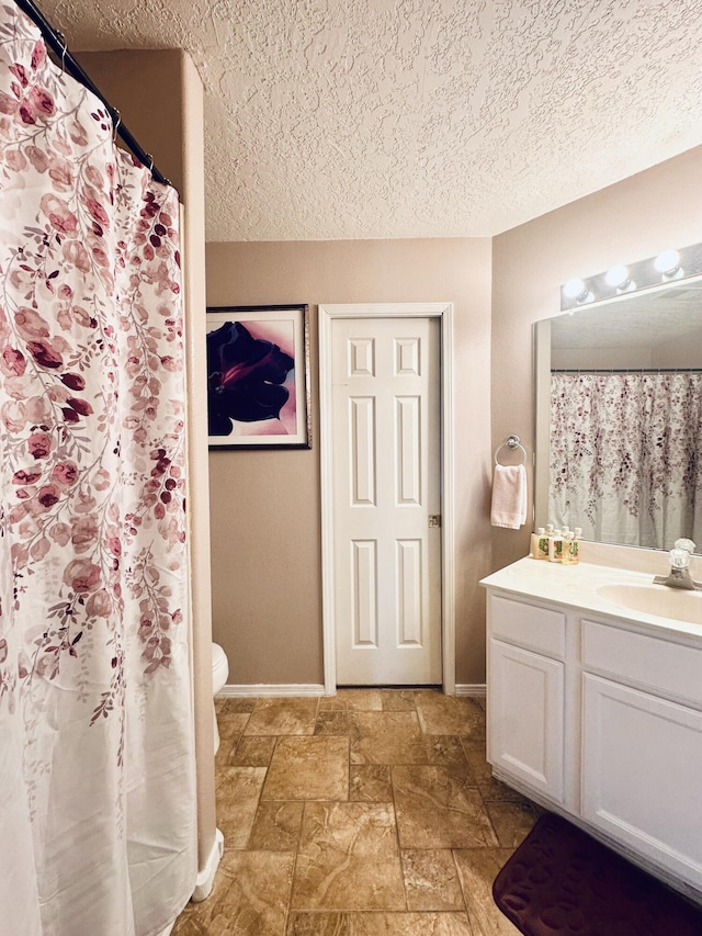 full bath featuring baseboards, vanity, stone tile floors, and a textured ceiling