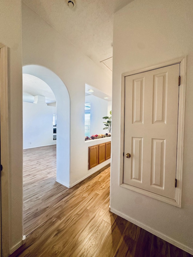 corridor with arched walkways, baseboards, and light wood finished floors