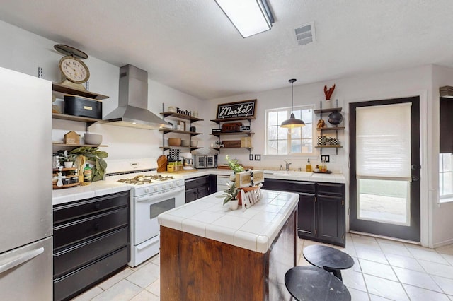 kitchen with tile counters, stainless steel appliances, exhaust hood, and open shelves