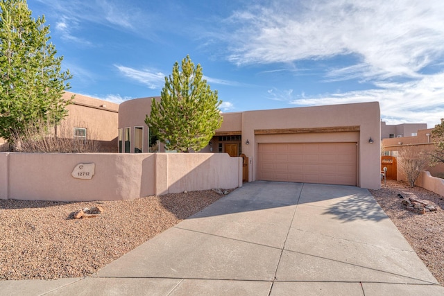 adobe home featuring concrete driveway, fence, an attached garage, and stucco siding