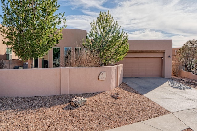 pueblo-style home featuring a garage, fence, concrete driveway, and stucco siding