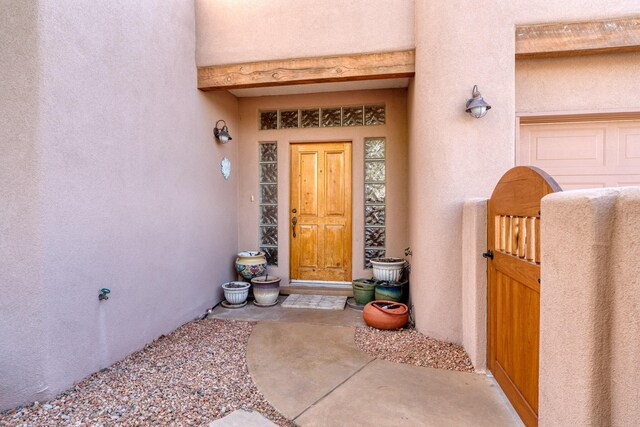 entrance to property featuring a garage, a gate, and stucco siding