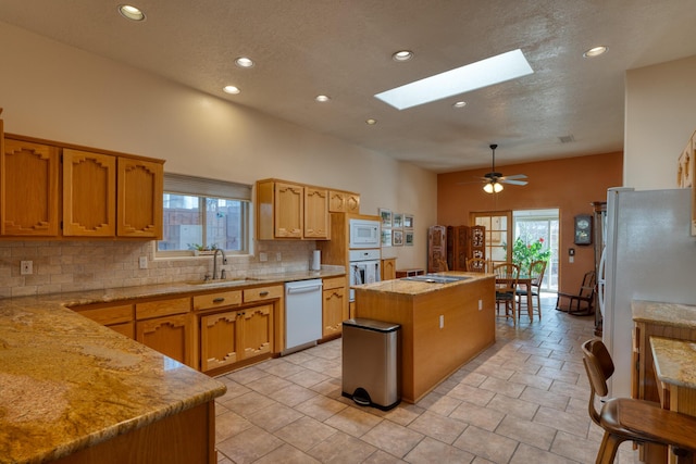 kitchen with white appliances, tasteful backsplash, a skylight, a kitchen island, and a sink