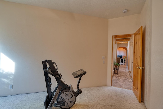 workout room with arched walkways and light colored carpet