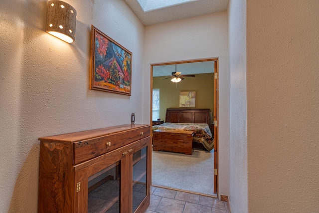 hallway featuring a textured wall, a skylight, light tile patterned flooring, and light colored carpet